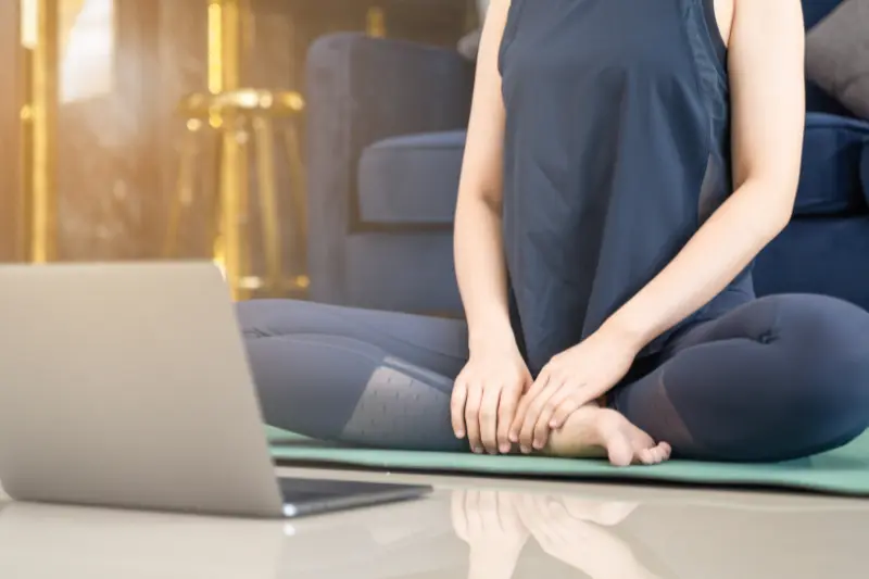 Femme assise sur un tapis de yoga devant un ordinateur à la maison