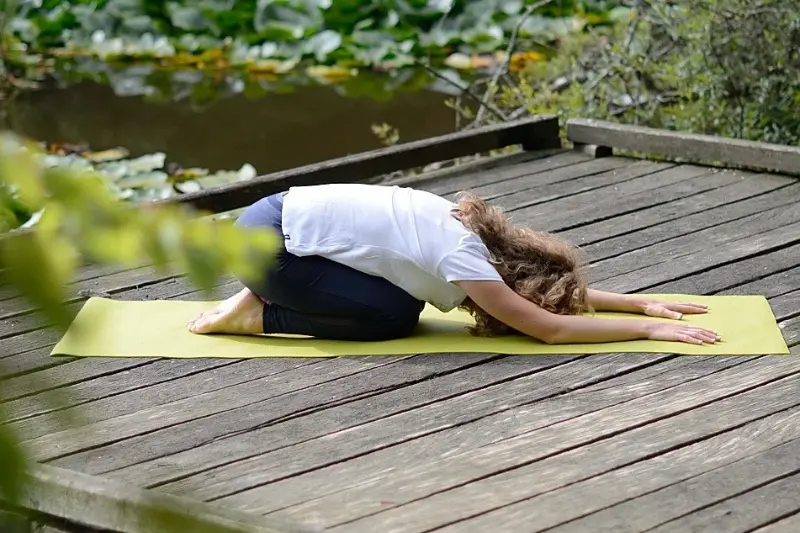 Femme pratiquant la posture de l’enfant sur un tapis de yoga en extérieur
