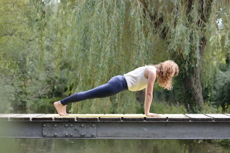 Femme pratiquant la posture de la planche sur un tapis de yoga en extérieur